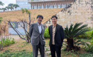 沖縄高専の校内で写真を撮るUSP研究所の當仲代表と、ritaの新潟代表